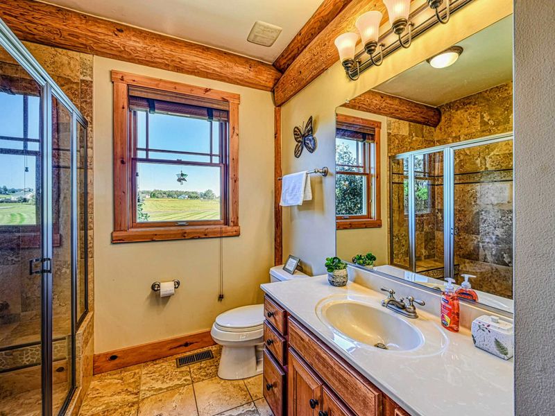 Indulge in this charming bathroom featuring natural wood accents, a spacious glass-enclosed shower, and picturesque views from the windows.
