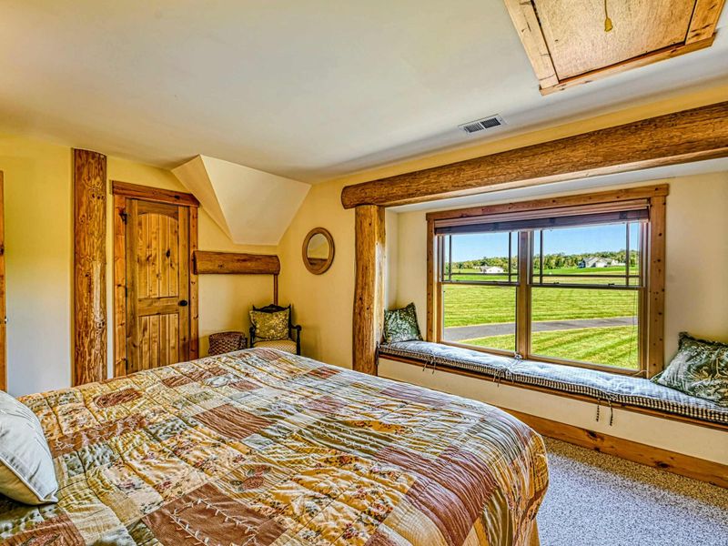 Relax in this cozy bedroom featuring rustic wood accents, a comfortable bed, and a charming window seat with scenic views.