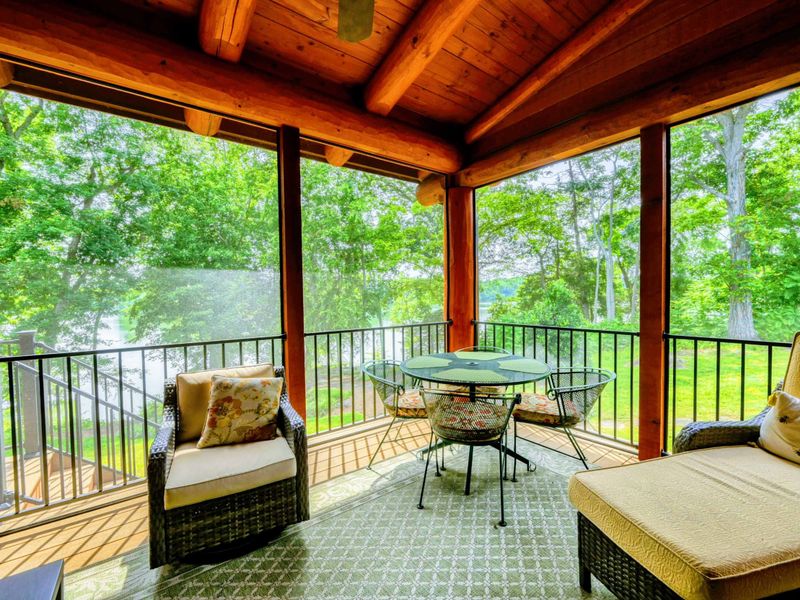 Exterior - Side view of the timber frame home showcasing the upper balcony, log construction, and expansive green lawn.