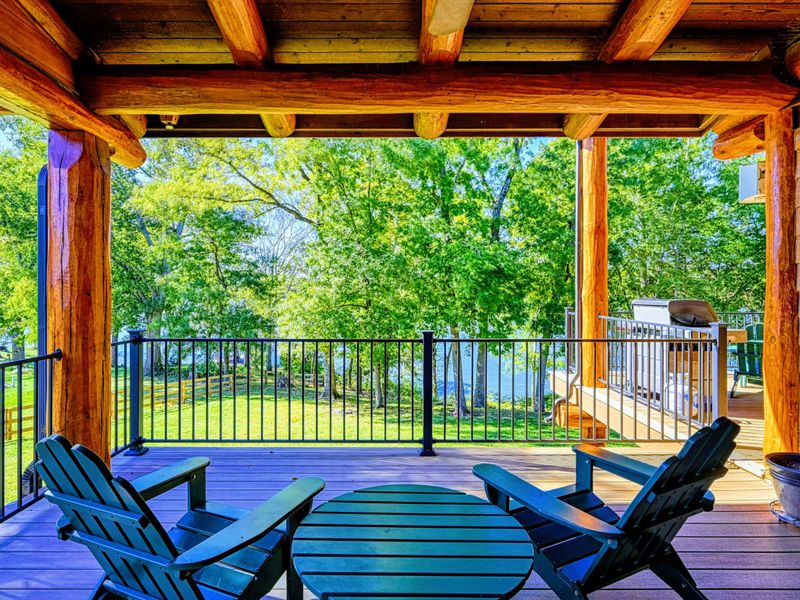 Relax on this charming covered deck featuring Adirondack chairs, a serene view of the lush greenery, and a cozy ambiance perfect for outdoor enjoyment.