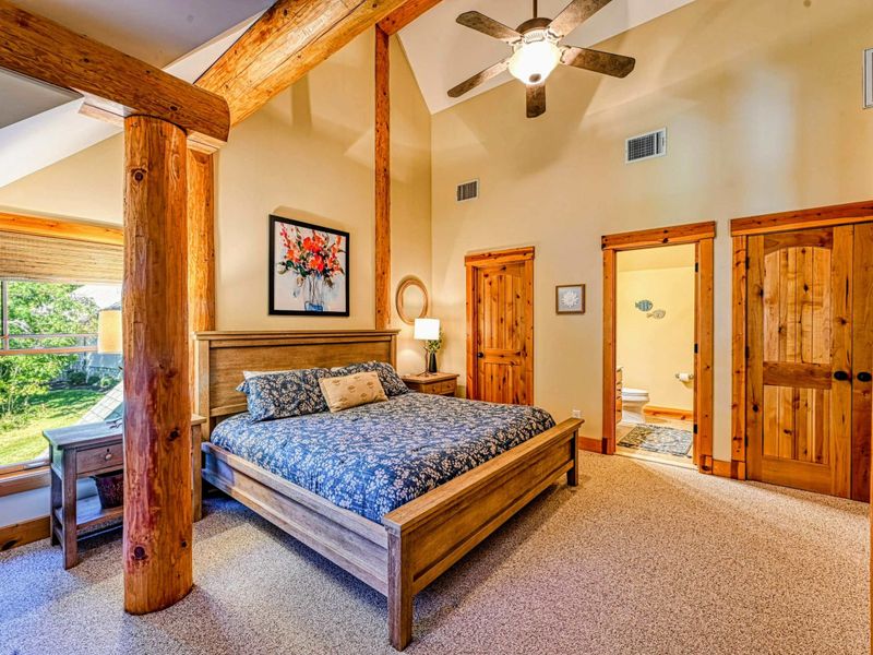 Retreat to this spacious and elegant bedroom featuring vaulted ceilings, rustic wooden beams, and thoughtfully curated decor for a cozy stay.