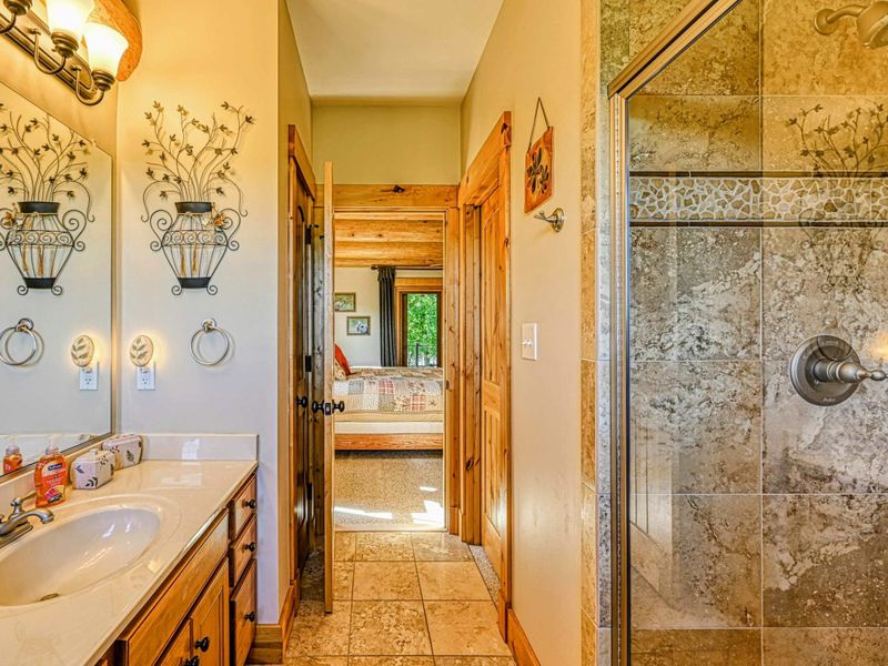 Indulge in this charming bathroom featuring natural wood accents, a spacious glass-enclosed shower, and picturesque views from the windows.