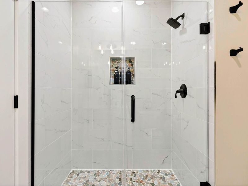 Bathroom 2 - Walk-in shower with marble tile, pebble floor, and matte black fixtures.