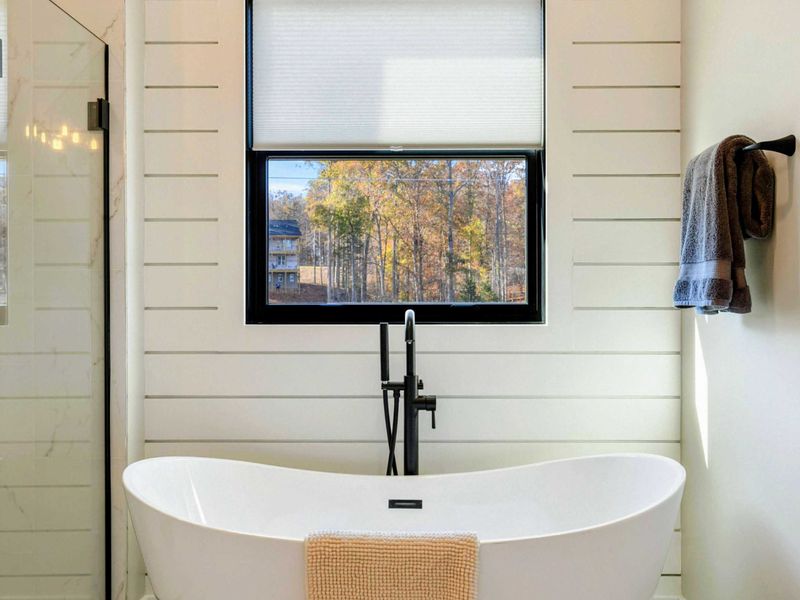 Primary Bath - Freestanding tub positioned beside a window with wooded views.