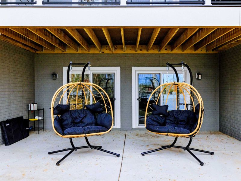 Cozy covered patio featuring two hanging chairs with plush cushions, perfect for relaxing in a serene outdoor setting.