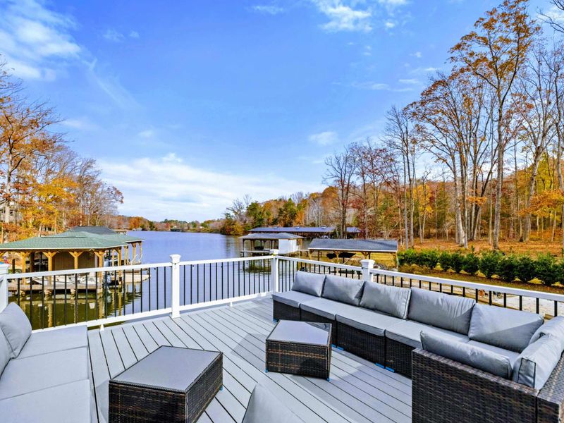 Spacious outdoor deck with comfortable seating, lounge chairs, and scenic views of a wooded area and water.