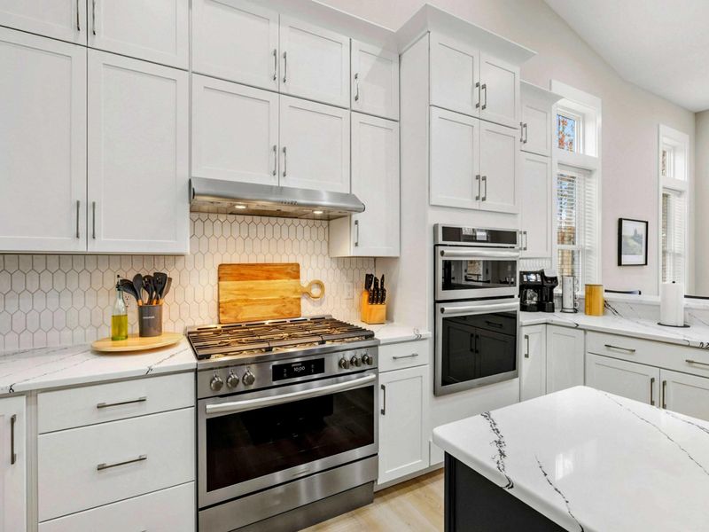 Spacious modern kitchen with white cabinetry, a central navy island, stainless steel appliances, and large windows offering scenic views.