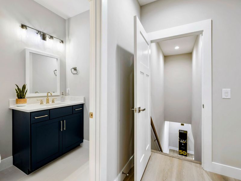 Stylish half bathroom with a navy vanity and gold fixtures, located near a staircase leading to the lower level.