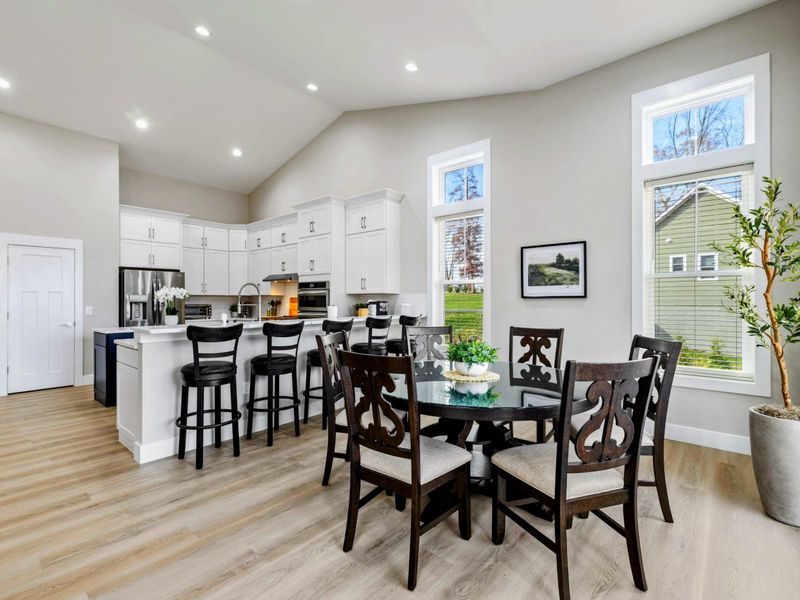 Open dining area with a stylish round table, adjacent to a modern kitchen with a large island and ample natural light from tall windows.