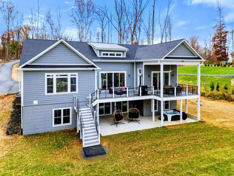 Modern lakeside home with an expansive deck, covered patio, hanging chairs, and a hot tub, perfect for relaxing and enjoying the outdoors.