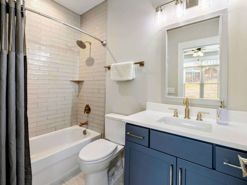 Modern bathroom featuring a tiled shower and tub combination, navy vanity with a sleek countertop, and stylish gold fixtures.