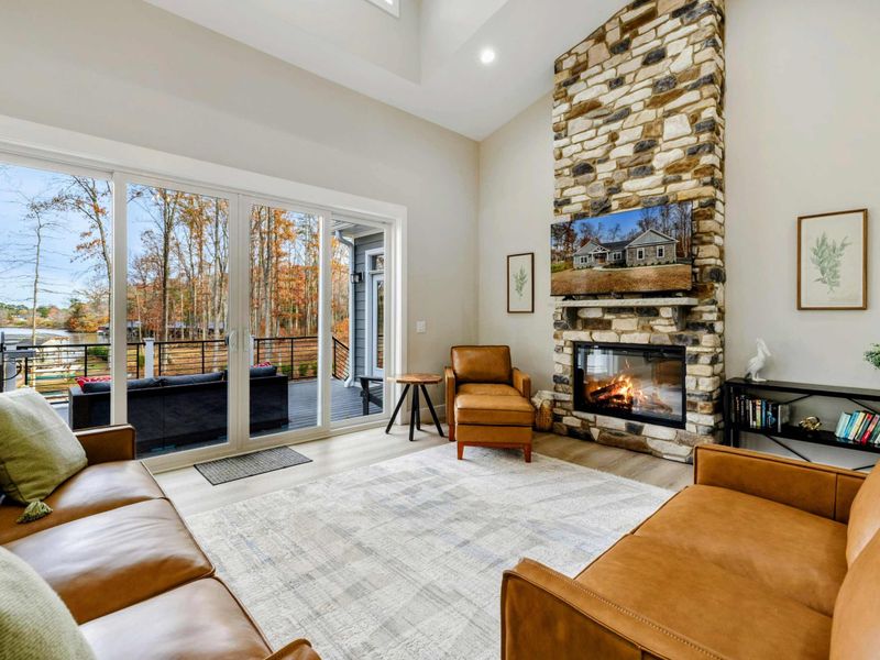Spacious living room with a stone fireplace, leather seating, and large sliding doors opening to a scenic outdoor deck.