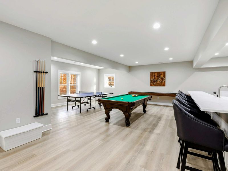 Spacious game room featuring a pool table, ping pong table, shuffle board, and bar seating, perfect for fun and relaxation.