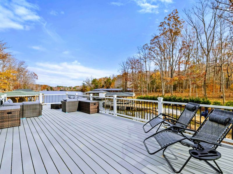 Spacious outdoor deck with comfortable seating, lounge chairs, and scenic views of a wooded area and water.