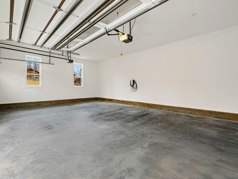 Spacious two-car garage with clean concrete flooring, natural light from windows, and an electric vehicle charging station.