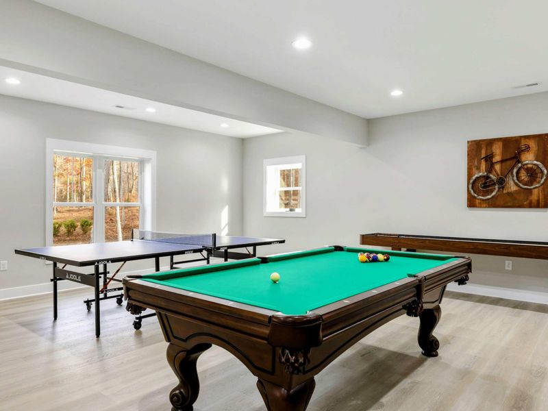 Spacious game room featuring a pool table, ping pong table, shuffle board, and bar seating, perfect for fun and relaxation.