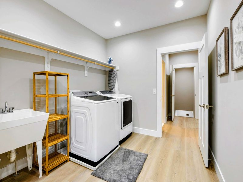 Spacious laundry room with modern washer and dryer, a utility sink, shelving, and stylish decor.