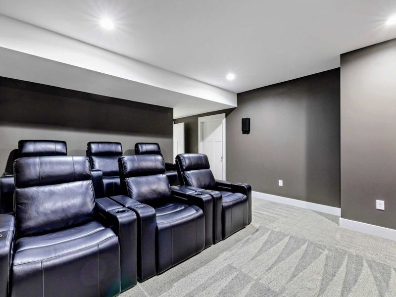 Enjoy a cozy and modern home theater experience with plush recliner seating and a large wall-mounted screen in this entertainment room.
