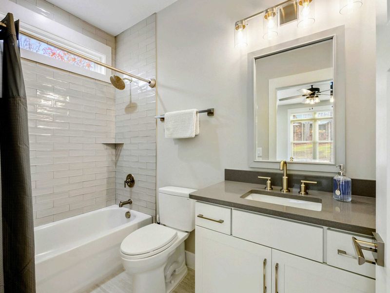 Modern bathroom with a tiled shower and tub combination, sleek white vanity, and stylish gold fixtures.