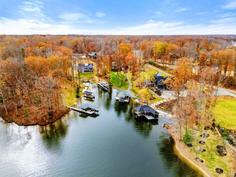 Aerial view of a serene lakeside property featuring private docks, boat slips, and lush autumn foliage in a peaceful wooded setting.