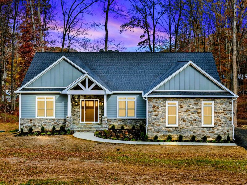 Charming modern home with a stone and siding exterior, a welcoming front porch, and a spacious yard surrounded by trees.
