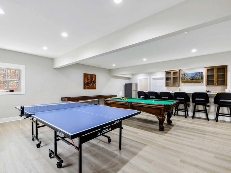 Entertainment room with a ping pong table, pool table, shuffleboard, and a bar area with seating, ideal for group activities and relaxation.