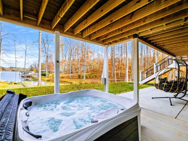 Covered patio with a bubbling hot tub, hanging chairs, and scenic views of the lake and surrounding trees.