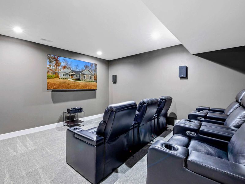 Enjoy a cozy and modern home theater experience with plush recliner seating and a large wall-mounted screen in this entertainment room.
