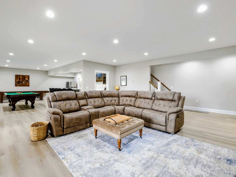 Lower-level entertainment space featuring a plush sectional sofa, pool table, and arcade game, ideal for relaxation and fun.