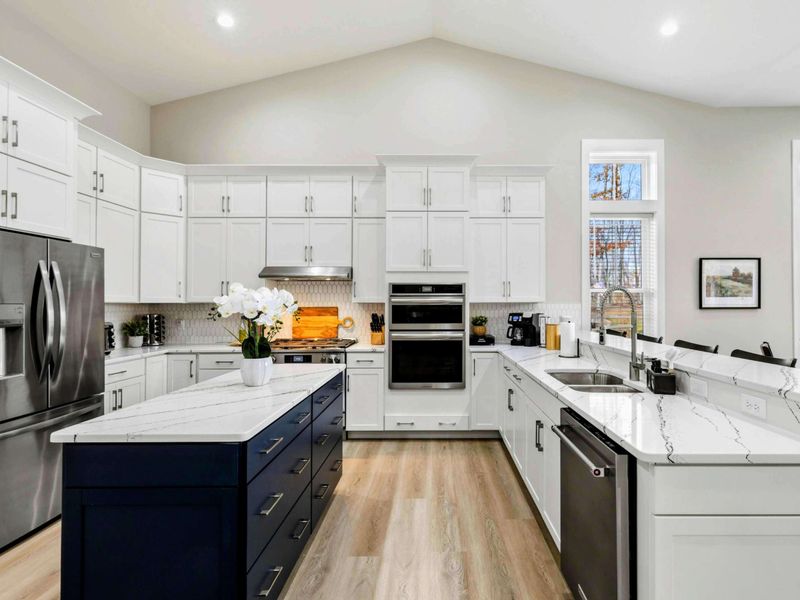Bright open-concept kitchen and dining area with white cabinets, a navy island, and large windows providing natural light and scenic views.
