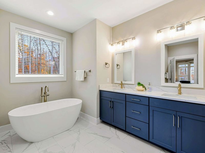 Luxurious en suite bathroom with a freestanding soaking tub, double vanity with navy cabinets, a walk-in shower, and elegant finishes.