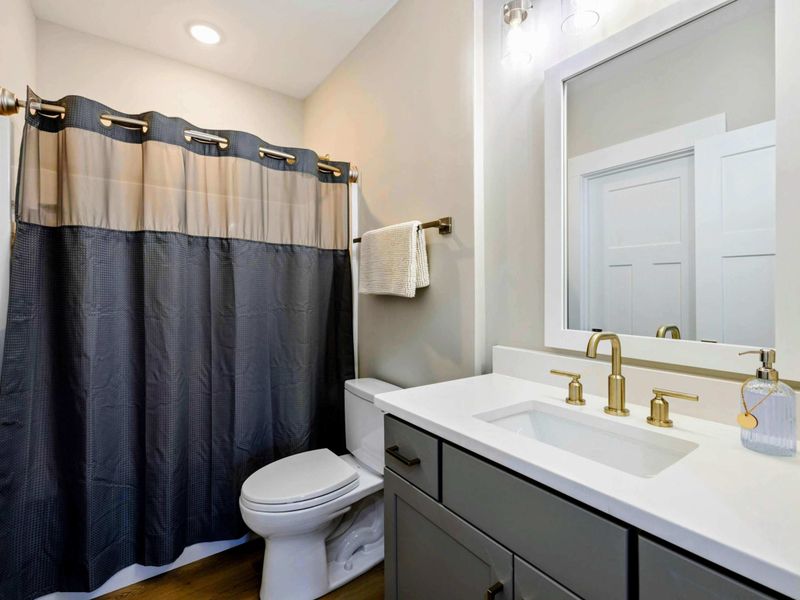 Modern bathroom with a sleek vanity, gold fixtures, and a shower-tub combination with a stylish curtain.