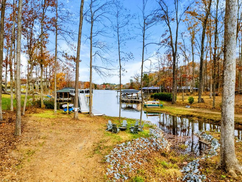 Lakeside retreat with Adirondack chairs around a fire pit, a private boat slip, paddleboards and kayaks in a peaceful wooded setting.