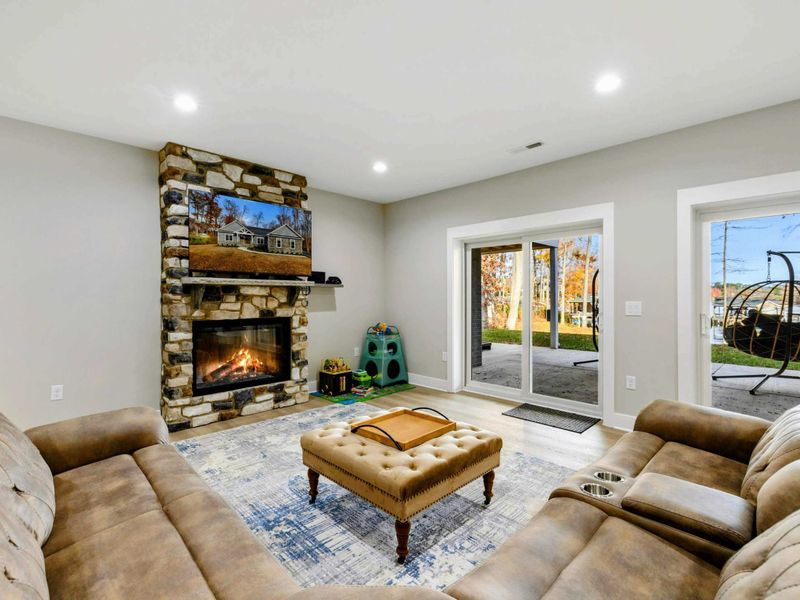 Cozy lower-level living space with a large sectional sofa, a stone fireplace, and a designated play area for kids.