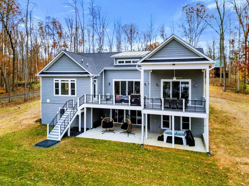 Modern lakeside home with an expansive deck, covered patio, hanging chairs, and a hot tub, perfect for relaxing and enjoying the outdoors.