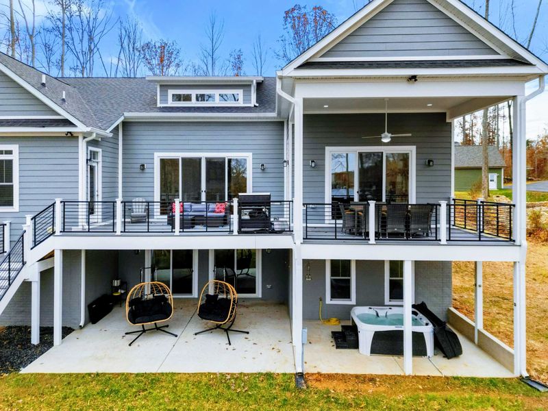 Modern lakeside home with an expansive deck, covered patio, hanging chairs, and a hot tub, perfect for relaxing and enjoying the outdoors.