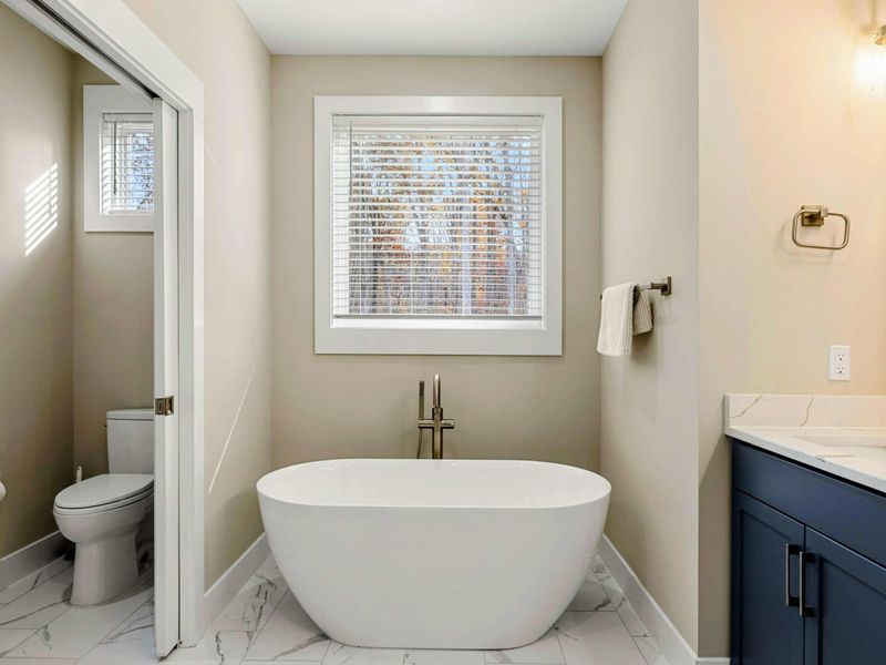 Luxurious en suite bathroom with a freestanding soaking tub, double vanity with navy cabinets, a walk-in shower, and elegant finishes.