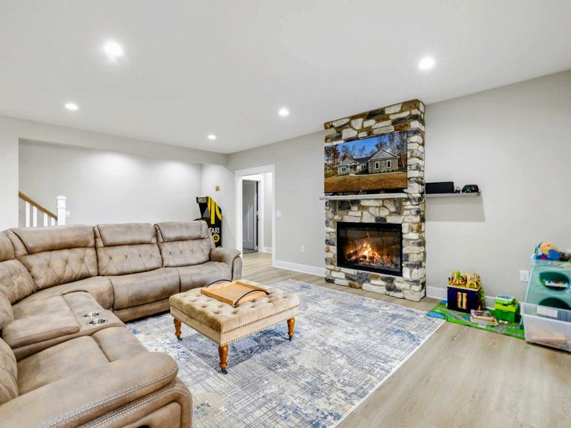 Cozy lower-level living space with a large sectional sofa, a stone fireplace, and a designated play area for kids.