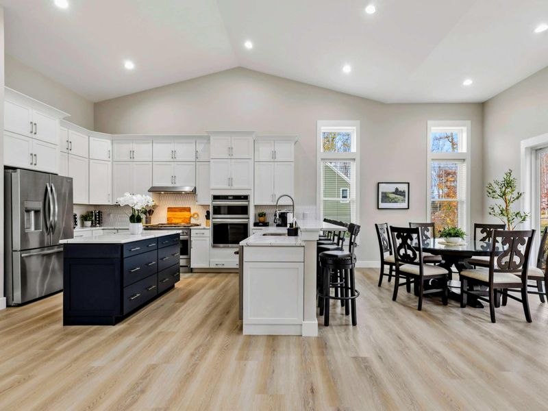 Bright open-concept kitchen and dining area with white cabinets, a navy island, and large windows providing natural light and scenic views.