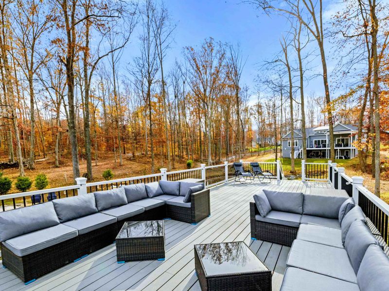 Spacious outdoor deck with comfortable seating, lounge chairs, and scenic views of a wooded area and water.