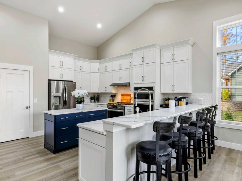 Bright open-concept kitchen and dining area with white cabinets, a navy island, and large windows providing natural light and scenic views.