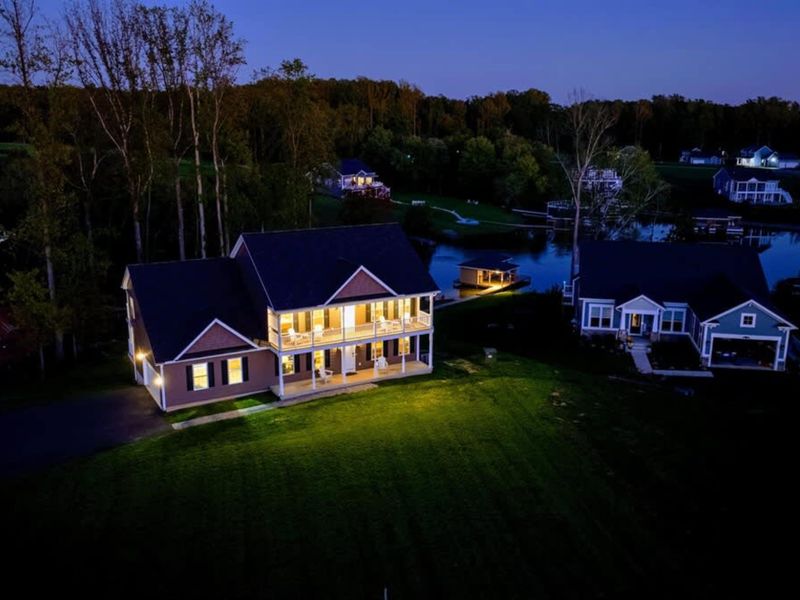 Exterior at Dusk - The house lit up at the end of a lake day, decks layered above each other, calm water beyond.