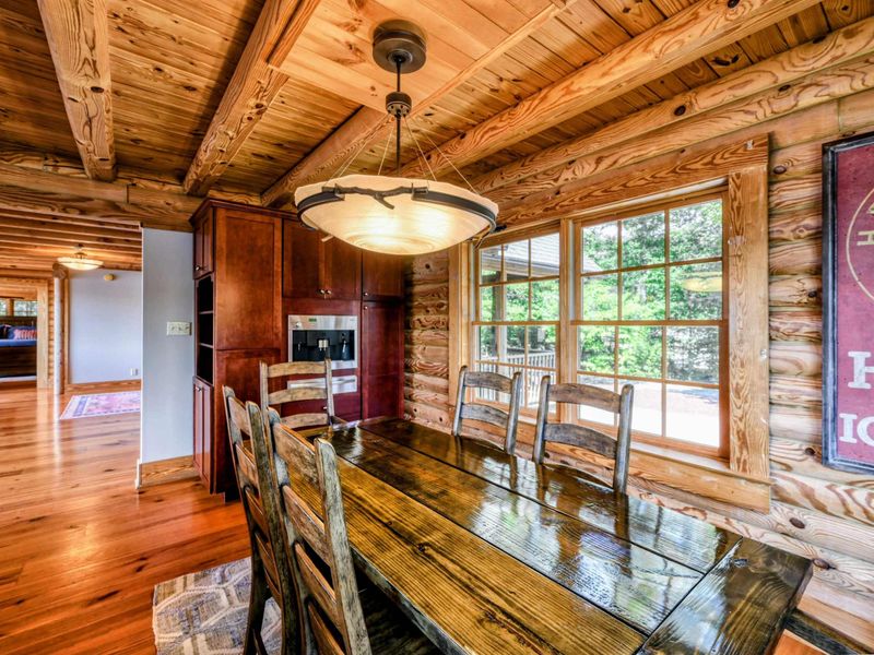 A beautifully designed kitchen with granite countertops, rich wood cabinets, and a cozy dining area framed by large windows and rustic decor.