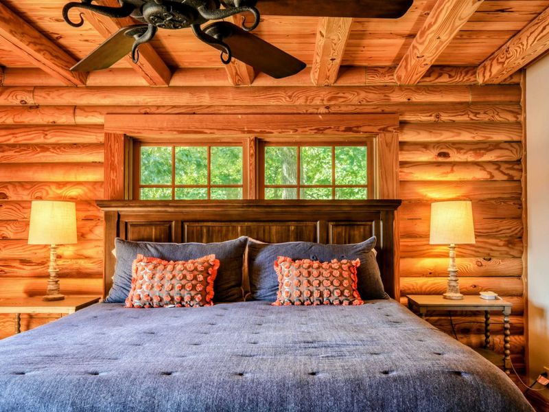 A close-up of the king-size bed highlights its luxurious linens, decorative pillows, and serene wood backdrop, with convenient access to an en suite bathroom.