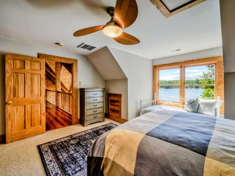 A bright and airy bedroom features a comfortable queen bed, a daybed with picturesque lake views, rustic accents, and an en suite bathroom for convenience.