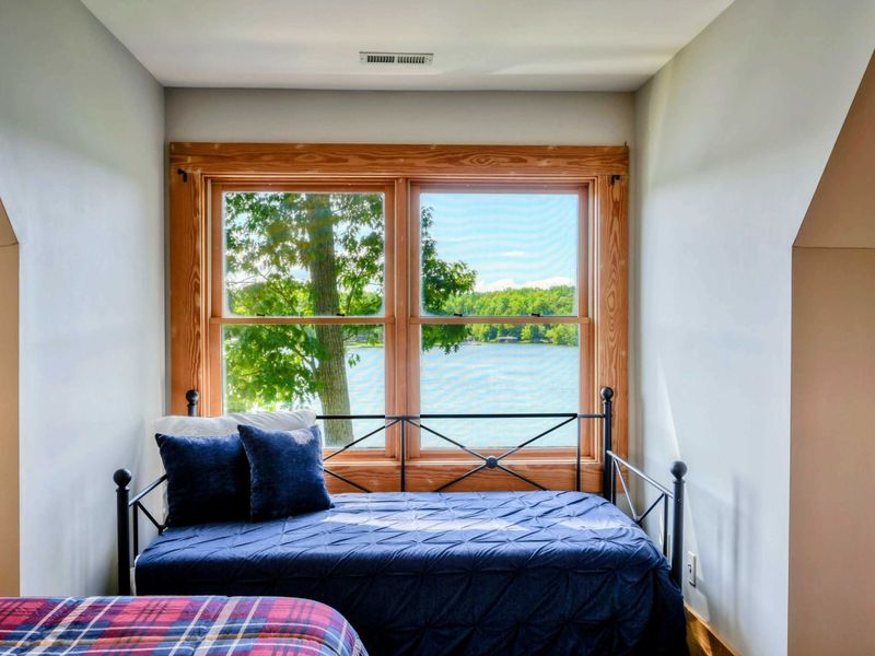 A charming bedroom with a queen bed, a daybed, and large windows offering stunning lake views, complemented by an en suite bathroom for added convenience.