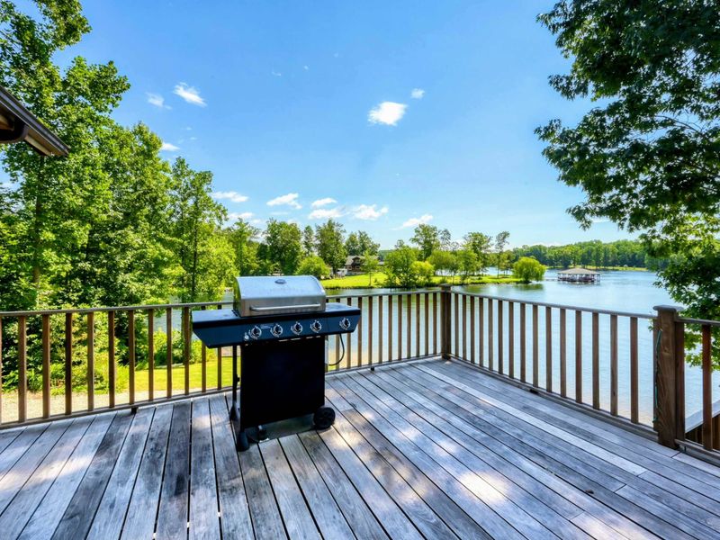 A serene lakeside view from a wooden deck with a grill and steps leading to a lush green lawn and private waterfront access.