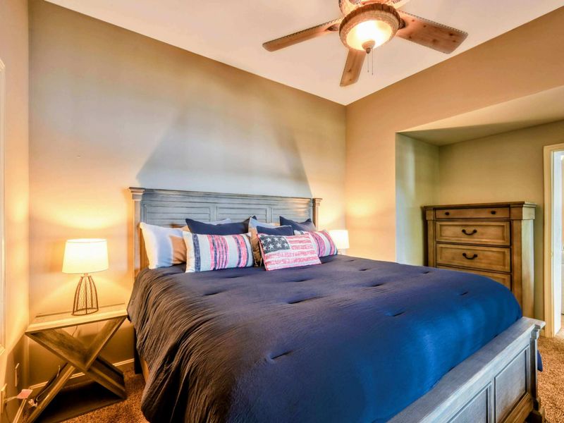 A stylish and cozy bedroom features a king-size bed with patriotic-themed decor, warm lighting, and a ceiling fan for added comfort.