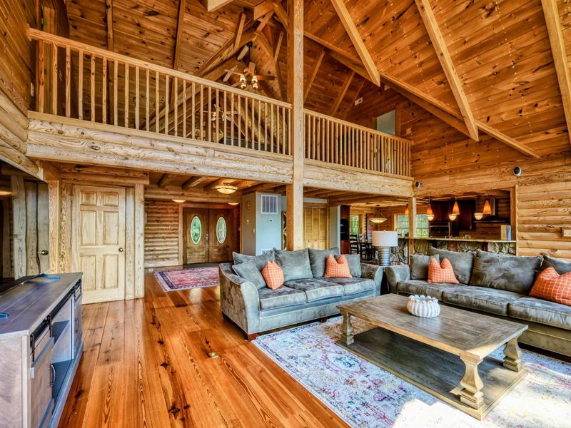 A beautifully crafted cabin interior features cozy seating, rich wooden finishes, and an open loft area overlooking the spacious living room.