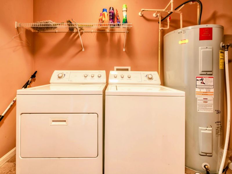 Convenient laundry room equipped with a washer, dryer, shelving for supplies, and a water heater.